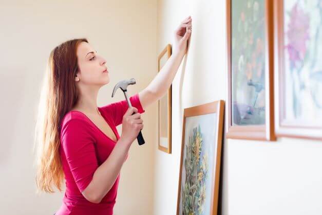 How To Display Artwork In Your Home 2 Lady nailing picture to wall