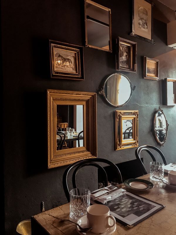 An opulent dining room with dark wall and lots of mirrors and artwork